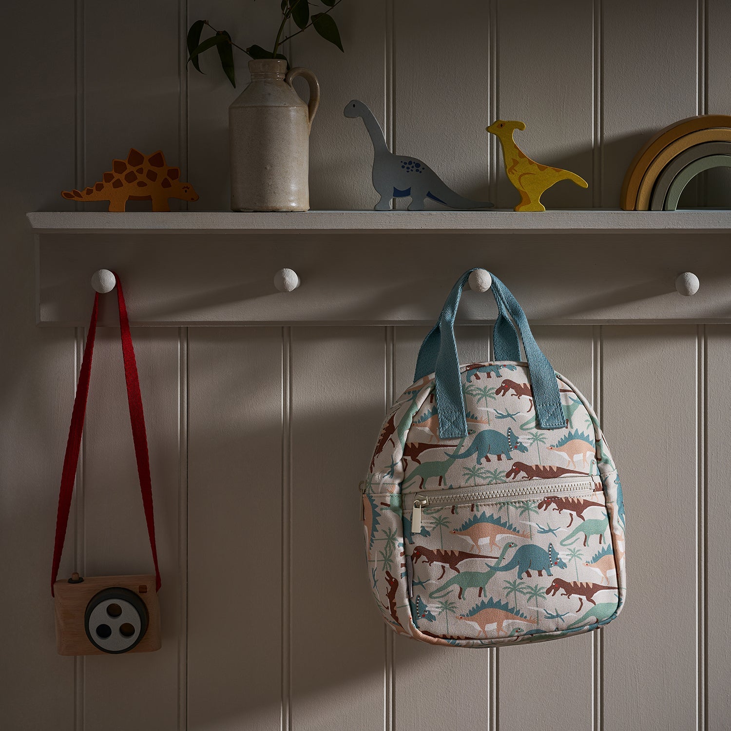 Dinosaur Camouflage Backpack by Sophie Allport hung up on a child's bedroom peg